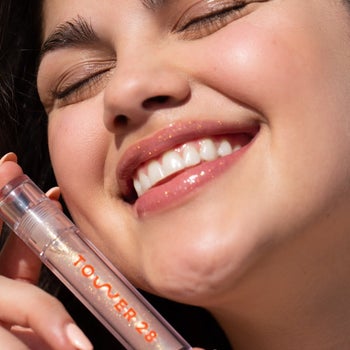 model wearing and holding the tube of lip gloss in the shade 