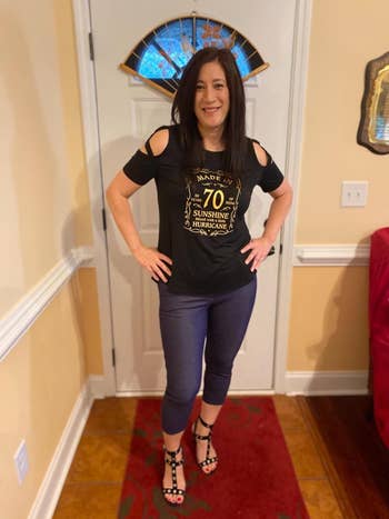 A reviewer wearing a T-shirt and blue capri jeans, standing in a room