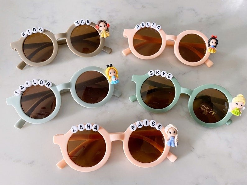 various sunglasses in pastel colors with kids names on them and a disney character