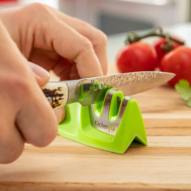 hands running a knife through a green knife sharpener