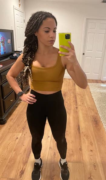 reviewer mirror selfie in gym clothes, wearing mustard colored workout crop top