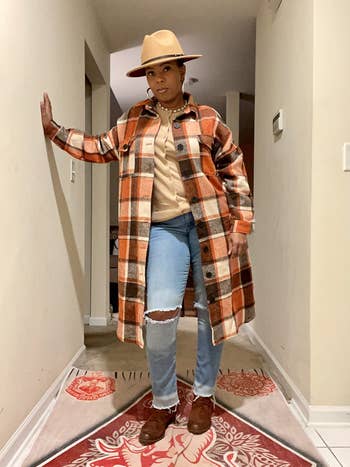 Person successful  hallway wearing a plaid coat, jeans, beige shirt, wide-brim hat, and boots