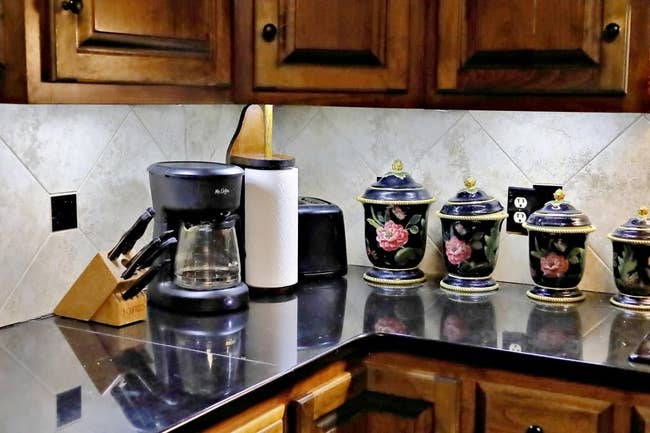 Kitchen countertop with a coffee maker, knife block, paper towel holder, and decorative jars