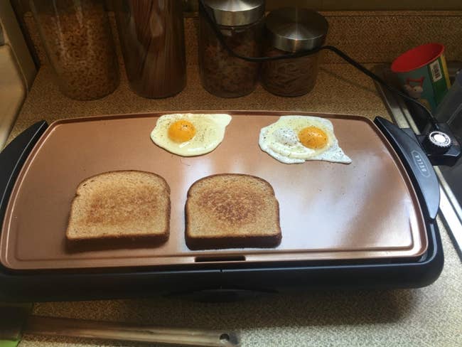 A reviewer's copper and black griddle with two pieces of toast and two eggs on it