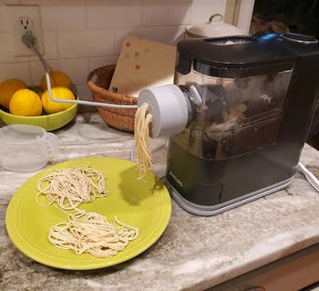 Electric pasta maker on a kitchen counter with freshly made noodles on a green plate