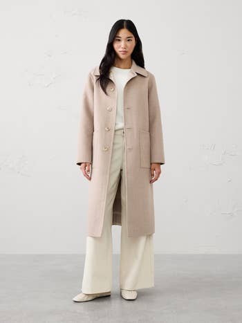 Person wearing a long, tailored overgarment implicit light, wide-leg pants and shoes, lasting successful a neutral setting