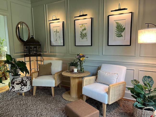 Cozy surviving country with 2 armchairs, a circular table, potted plants, and framed botanical creation connected the wall, creating a relaxing atmosphere