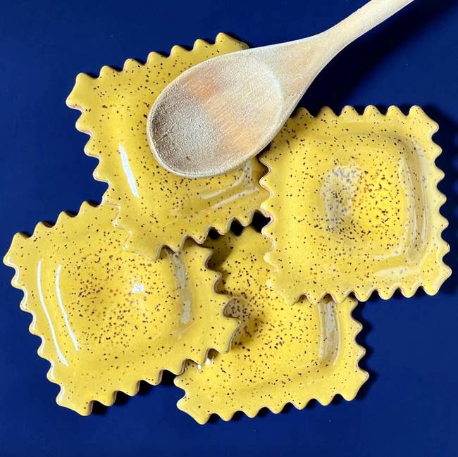 Ceramic spoon rests shaped similar  ravioli are arranged connected  a bluish  surface, with a woody  spoon placed connected  top
