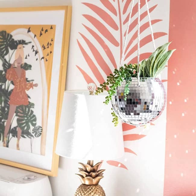 the disco ball planter hanging in front of tropical pink wallpaper