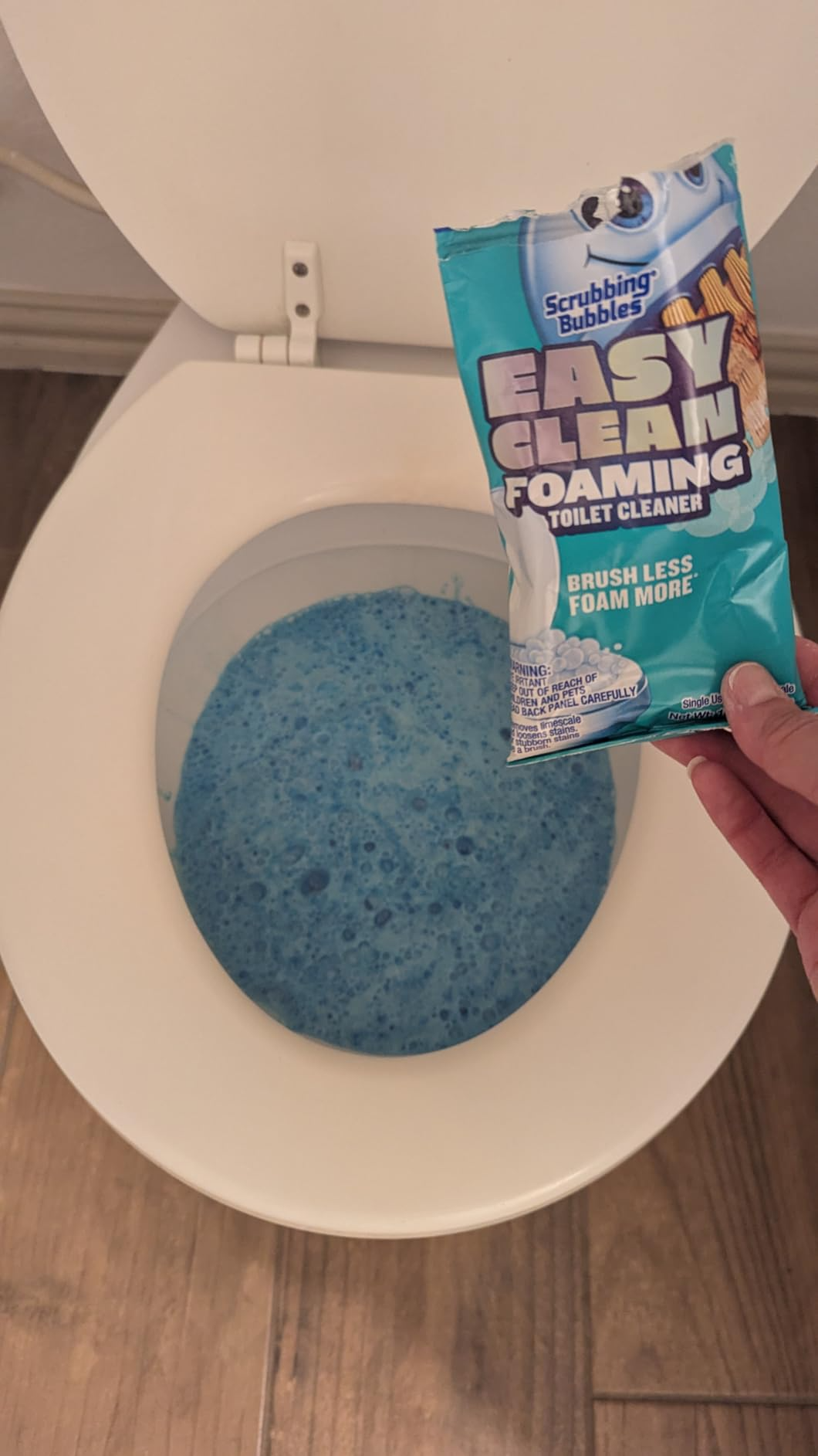 Package of foaming toilet cleaner is held supra  a toilet with bluish  foam inside