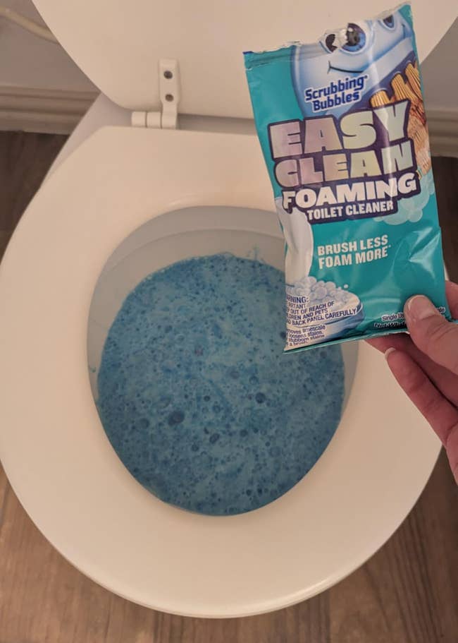 Package of foaming toilet cleaner is held supra a toilet with bluish foam inside
