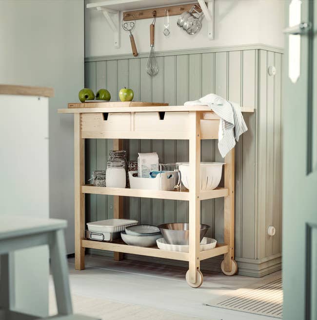 Wooden room  cart with drawers, unfastened  shelves holding dishes, bowls, and 3  greenish  apples connected  top, successful  a modern   room  setting