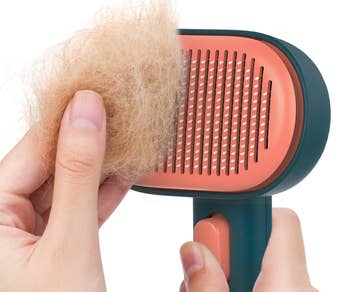 Pet grooming brush being cleaned, showing a clump of fur removed from the bristles with a hand