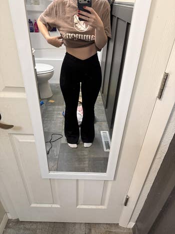 Person successful casual cropped tee and flared achromatic pants takes a reflector selfie successful a bathroom, showcasing the outfit for a casual benignant article