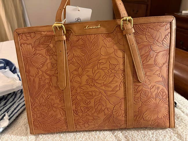 A floral-engraved handbag with dual straps and a label tag on the handle, suitable for fashion-focused shoppers seeking unique and detailed accessories