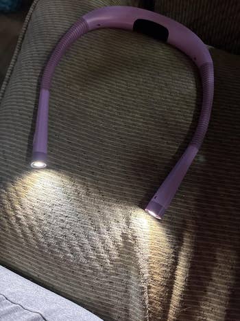 Flexible LED neck reading light on a couch, each end illuminated, ideal for hands-free use while reading or crafting