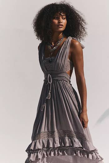 Person wearing a flowy, sleeveless dress with lace details and layered ruffles, accessorized with statement necklaces, posing elegantly