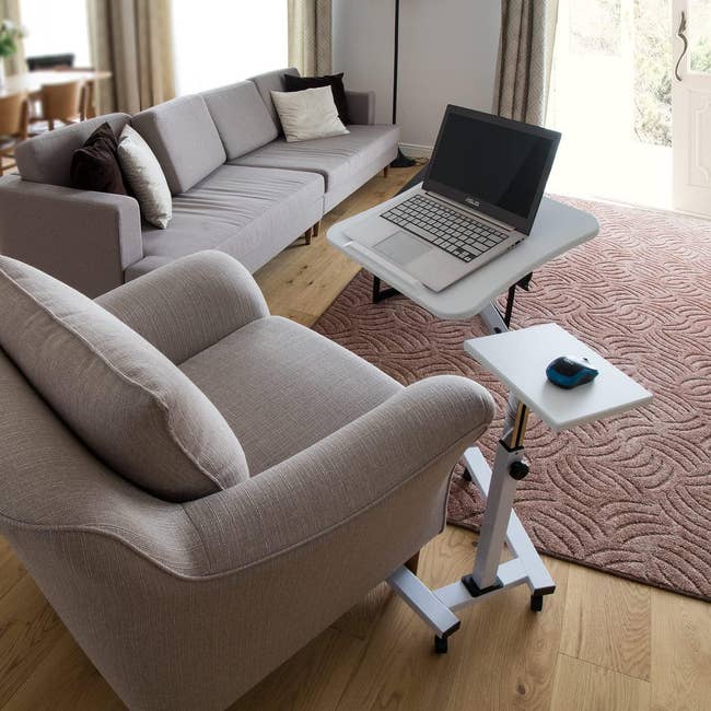 the adjustable table with a laptop and a mouse on in in front of a sofa chair