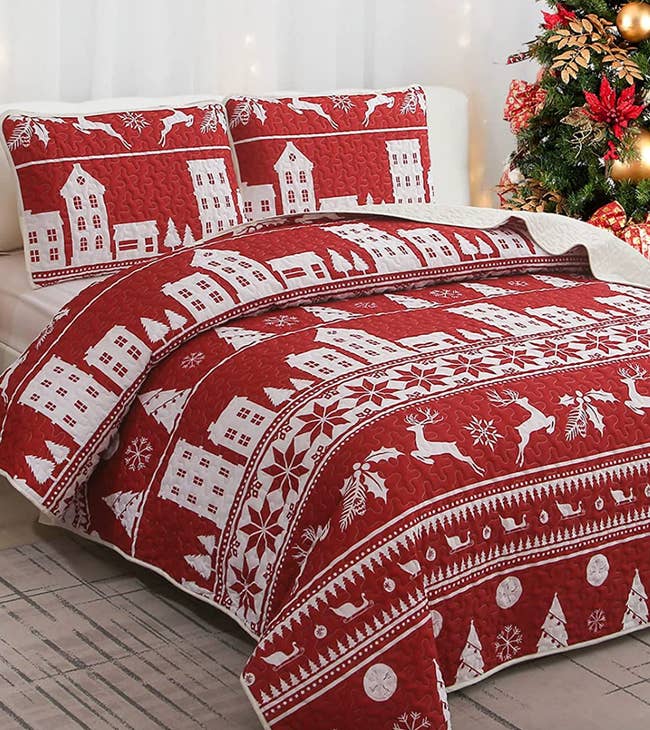 red and white quilt with sleighs, trees, and houses on a bed with patching pillow shams