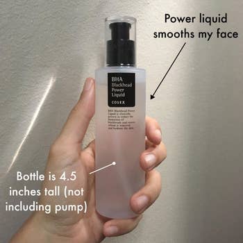 Hand holding a 4.5-inch tall COSRX BHA Blackhead Power Liquid bottle with text indicating its function to smooth the face by eliminating blackheads
