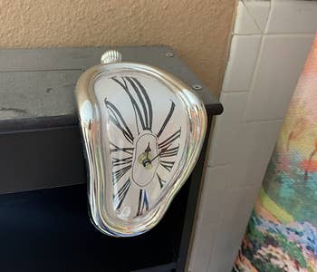 a reviewer photo of the melting clock on the edge of a mantel 