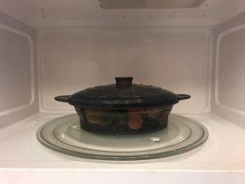 The black oval steamer and lid with veggies inside it sitting in a microwave