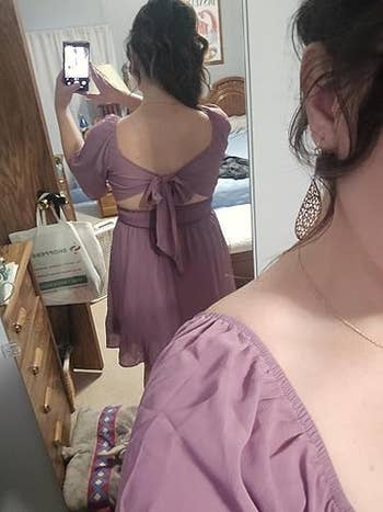 Person taking a mirror selfie in a room, showing the back of their lavender dress with a bow detail