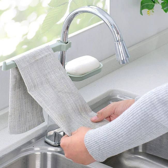 model grabbing towel hanging off green bar attached to sink nozzle, with another bar with soap tray attached below