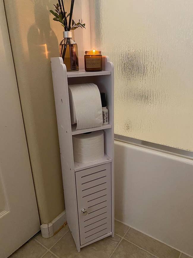 White bathroom caddy with rolls of toilet paper and a lit candle on top