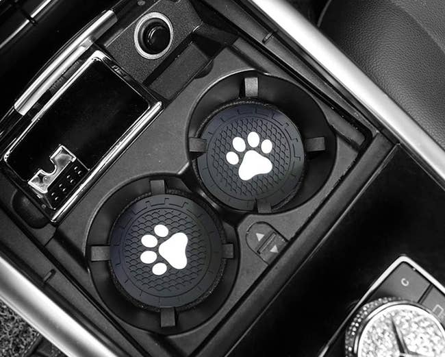 two silicone coasters with white paw prints on them in car cup holders