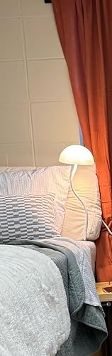 Bed with a textured quilt, a pillow, and a bedside lamp, acceptable   against closed curtains