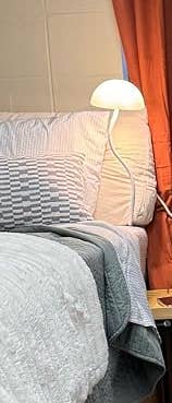 Bed with a textured quilt, a pillow, and a bedside lamp, acceptable against closed curtains