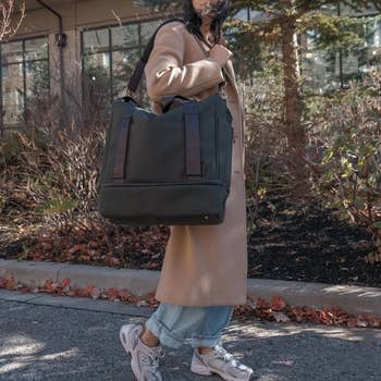 Person with oversized tote bag on shoulder, wearing a coat over casual clothes, partial view, focus on bag style
