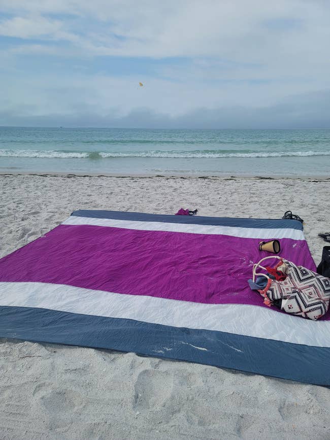 Beach blanket on sand with a bag and speaker, ocean in the background, no people present