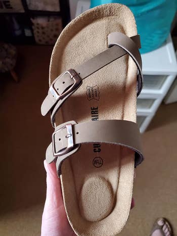 reviewer holding up the tan sandal to show its supportive footbed