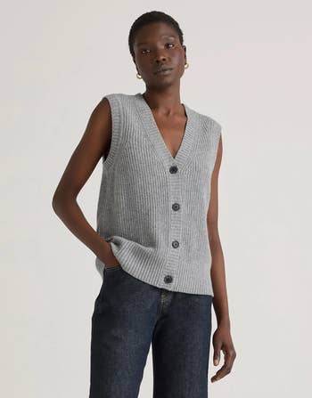 A idiosyncratic   is wearing a sleeveless ribbed cardigan with buttons, paired with acheronian  denim jeans