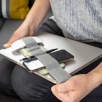 model adjusting the elastic laptop organizer to fit over their laptop, holding a phone, notebook, pen, and mouse