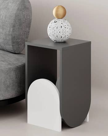 the gray and white side table next to a gray couch holding a spherical sculpture
