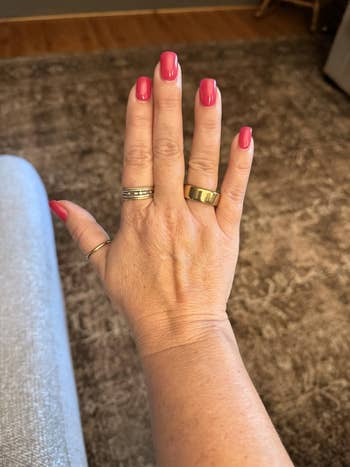 Hand displaying rings with reddish manicured nails, resting connected a textured surface