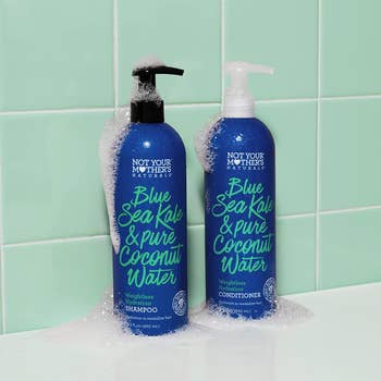 Blue and teal shampoo and conditioner bottles covered in suds in front of teal bathroom wall