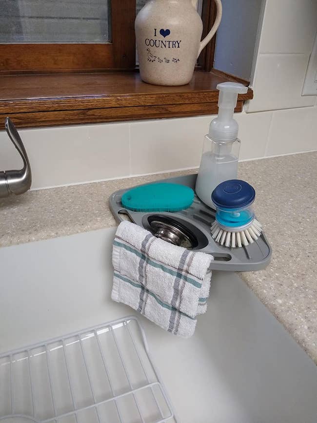 Reviewer's gray sink tray holding a sponge, brush, and soap with a towel hanging from it