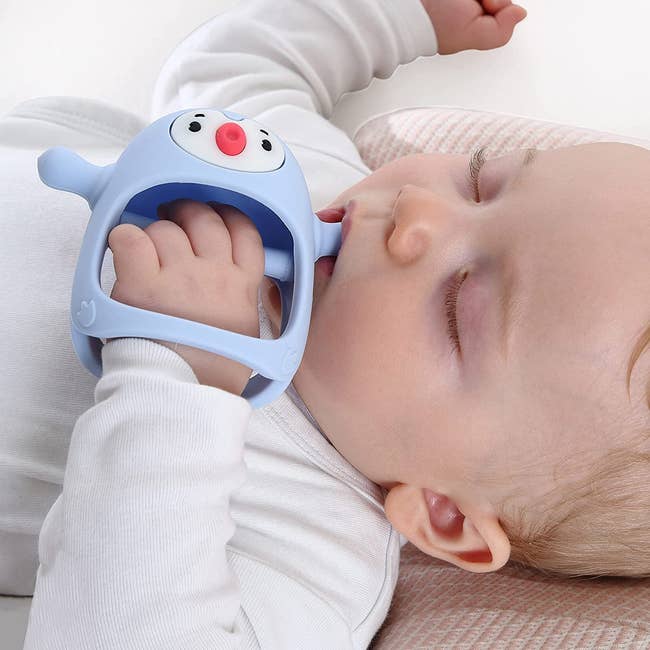 Baby holding a penguin shaped teether with a grip for their hand 