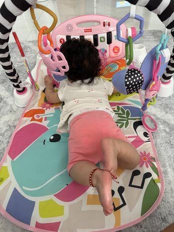 Baby playing connected  an enactment   gym mat with attached toys, a keyboard, and colorful designs