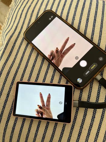 Smartphone and camera screens show a manus making a bid sign, highlighting dual gadget use