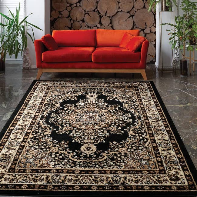 A traditional black and beige area rug on a floor with a red couch behind it