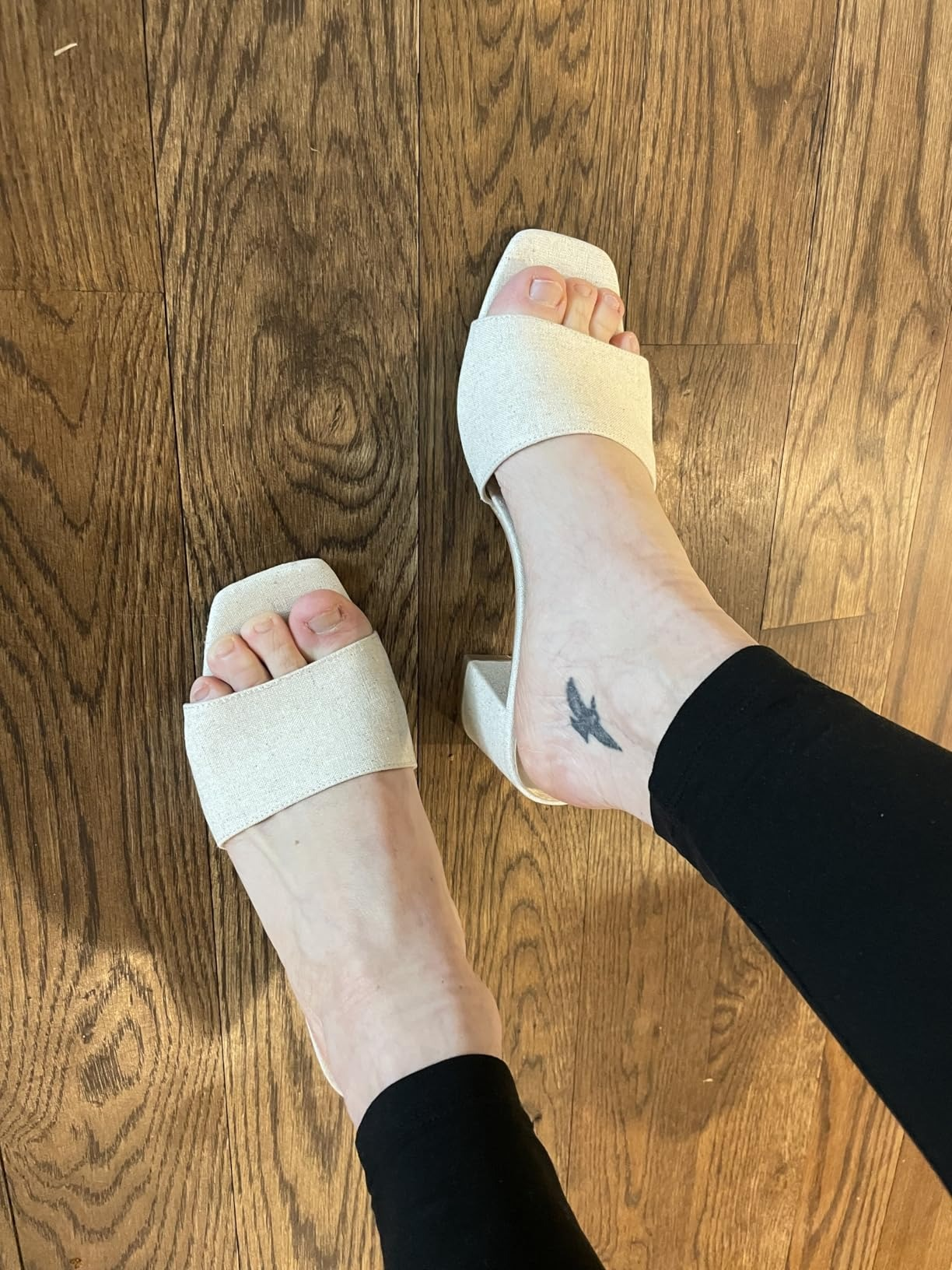 Person wearing stylish open-toe heeled sandals, showcasing a tiny  tattoo connected  the ankle, lasting  connected  a woody  floor