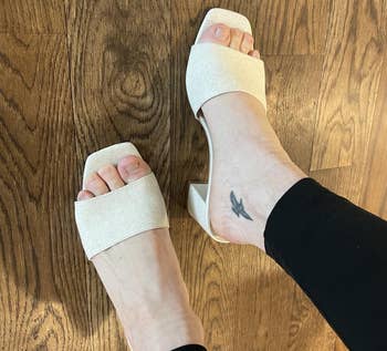 Person wearing stylish open-toe heeled sandals, showcasing a tiny tattoo connected the ankle, lasting connected a woody floor