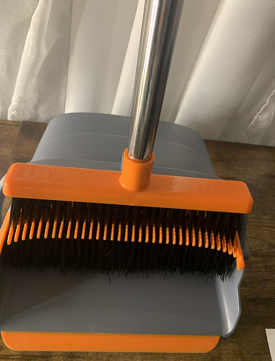 An orange broom with a gray dustpan with slotted edges to clean the bristles of the broom 