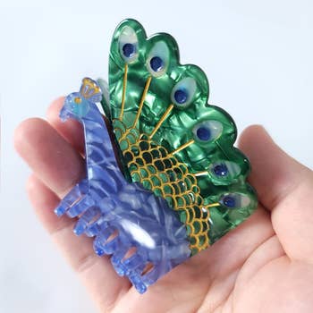 peacock-shaped hair claw clip in the palm of a model's hand