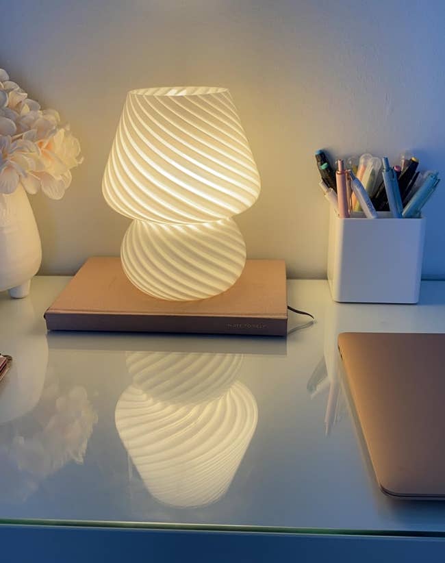 Spiral table lamp on, notebook and pen holder on desk, subtle lighting for ambience or reading